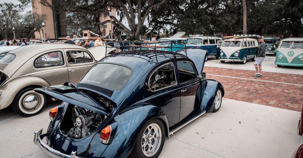 A vintage Volkswagen Beetle with an open trunk showcased at a classic car show outdoors.